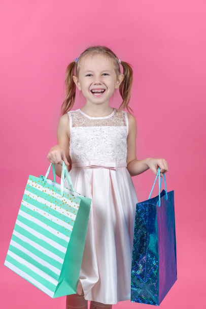Adorable 6 year caucasian girl holding shopping bags against pink background with copy space. - Фото, зображення