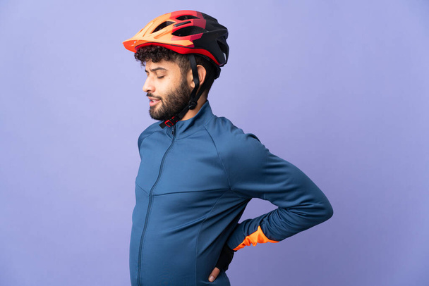 Joven ciclista marroquí aislado sobre fondo púrpura sufriendo de dolor de espalda por haber hecho un esfuerzo - Foto, Imagen