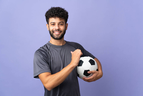Guapo marroquí joven jugador de fútbol hombre sobre aislado sobre fondo púrpura orgulloso y satisfecho de sí mismo - Foto, imagen