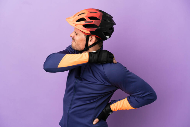 肩の痛みに苦しんでいる紫の背景に孤立した若いブラジルのサイクリストの男は努力をした - 写真・画像