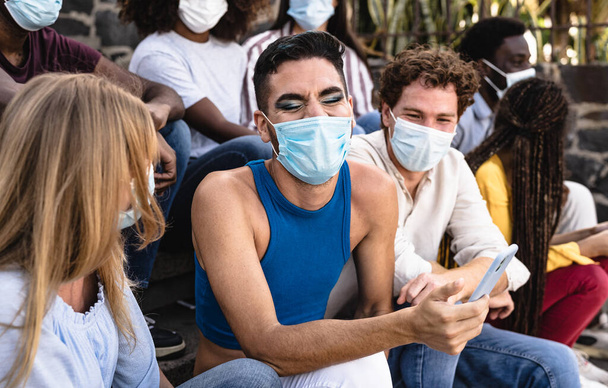 Junge multiethnische Freundesgruppe sitzt mit Chirurgenmaske auf urbanen Treppen - Millennial-Lifestyle-Konzept der Jugend - Foto, Bild