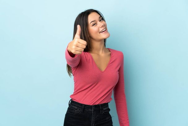 Teenager girl isolated on blue background with thumbs up because something good has happened - Foto, Imagem