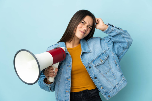 Teenager girl isolated on yellow background holding a megaphone and having doubts - Foto, Imagen