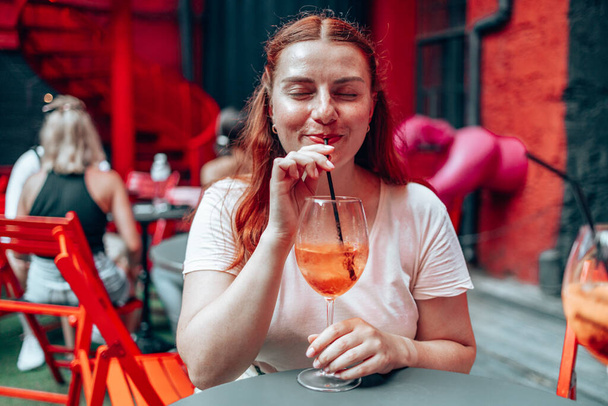 30 років щаслива жінка відпочиває і насолоджується келихом вина холодного коктейлю Aperol spritz на фоні ресторану
. - Фото, зображення