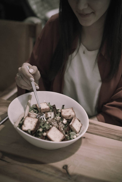 Portrait of attractive caucasian smiling woman eating salad, focus on hand and fork. - Photo, Image
