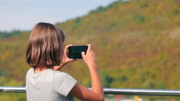 Adolescente menina tira fotos com um telefone celular enquanto viaja em um navio. A menina tira fotos em seu celular. - Filmagem, Vídeo