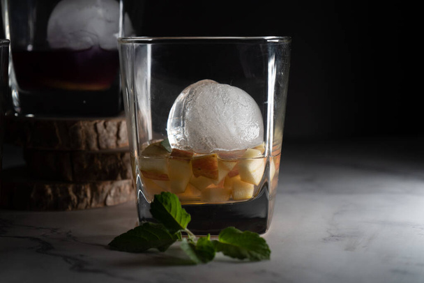 dois copos fileld com vinho infundido mulled gin rum vodka com esferas de gelo, fatias de fruta de maçã e folhas de hortelã mostrando o hobby de mulling para bebidas de celebração - Foto, Imagem