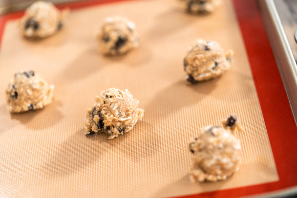 Scoops of cookie dough on a baking cheets to bake chewy oatmeal raisin cookies. - Fotó, kép