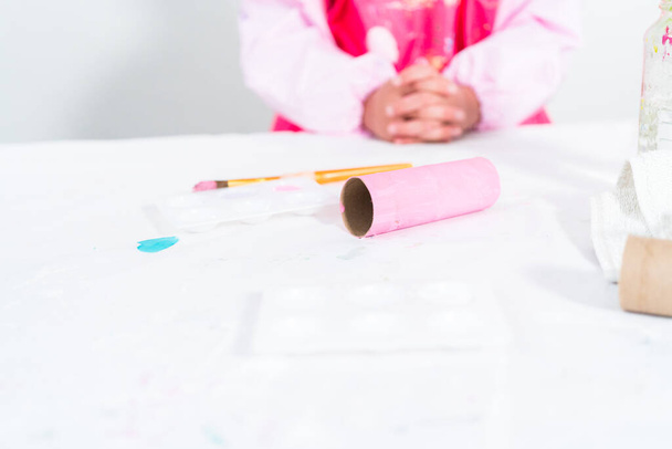 Маленькая девочка делает единорога из рулона туалетной бумаги и ремесленной бумаги. - Фото, изображение
