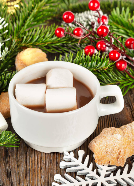 Hot chocolate or cocoa drink with marshmallow in a white cup, sweet homemade cookies and fir tree on a brown wooden background. Christmas and new year traditional food.  - Photo, Image