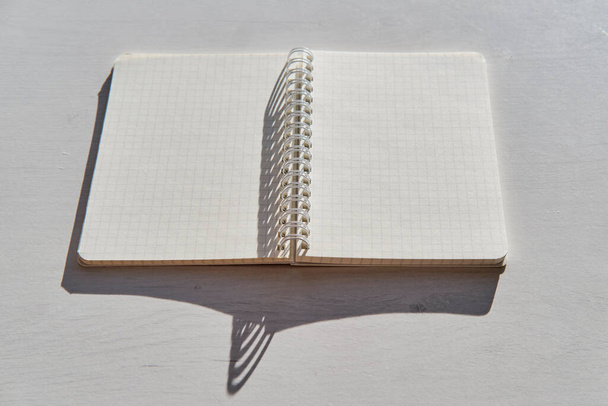 Otevřený prázdný zápisník na bílém stole v jasném slunečním světle, s tvrdými stíny. - Fotografie, Obrázek