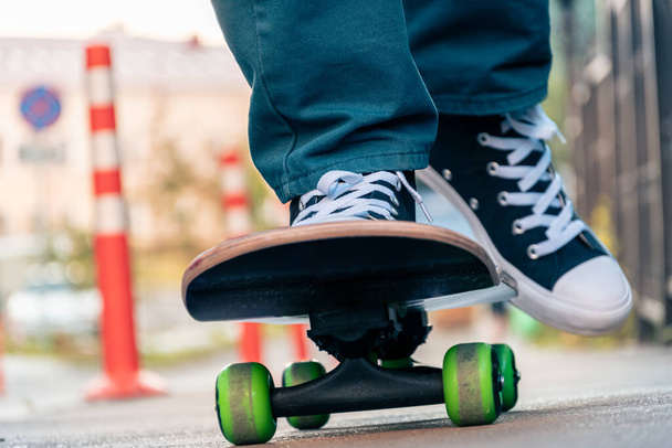Close-up of men's legs in jeans and sports shoes on a skateboard on a city street at sunset - 写真・画像