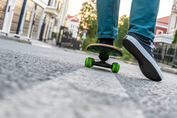 Close-up of men's legs in jeans and sports shoes on a skateboard on a city street at sunset - 写真・画像