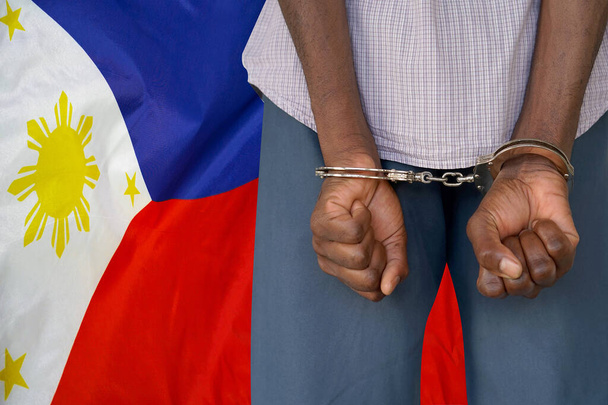 Uomo africano con le manette sullo sfondo della bandiera delle Filippine. Vista posteriore. Concetto di prigioni e corruzione nelle Filippine - Foto, immagini
