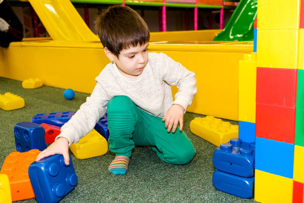 Bir anaokulu çocuğu oyun odasındaki büyük inşaat bloklarıyla, bir çocuk eğlence merkeziyle, kapalı bir oyun parkıyla oynar. - Fotoğraf, Görsel