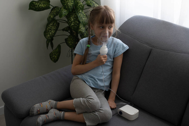 Enfant de neuf ans souffrant d'asthme allergique, inhalant ses médicaments à travers l'entretoise tout en regardant avec ses yeux fatigués - Photo, image