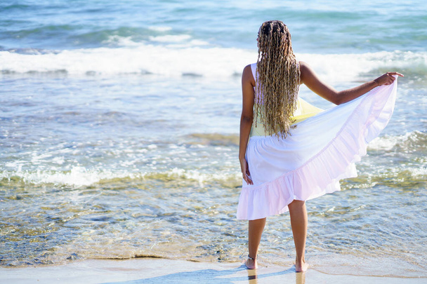 Chica negra caminando a lo largo de la orilla de la playa con un hermoso vestido largo. - Foto, Imagen
