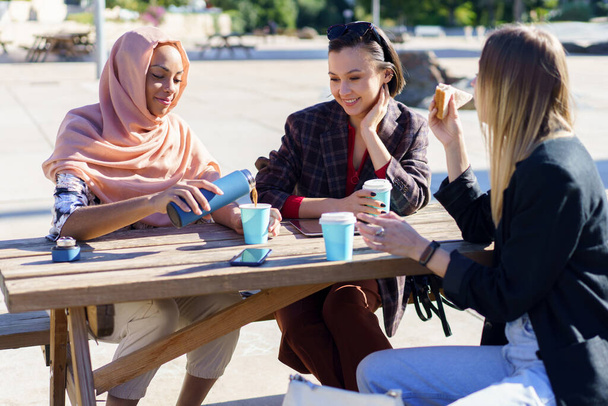 Positieve diverse vrouwen met koffiepauze aan tafel in het park - Foto, afbeelding