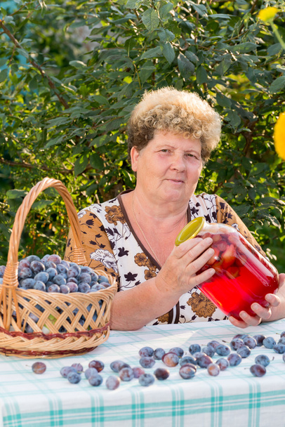 elderly woman with a jar of plum compote - Фото, зображення