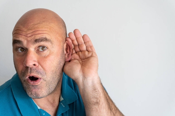 Portrait of middle-aged Caucasian man with hand behind ear listening to gossip, on white background - Photo, Image