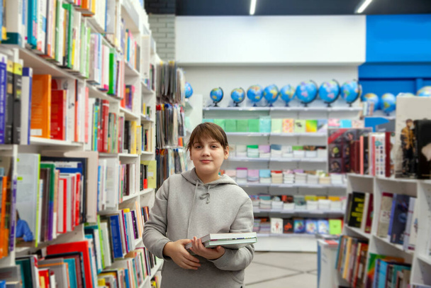 Έφηβο κορίτσι με γκρι κουκούλα που διαλέγει βιβλία στο κατάστημα - Φωτογραφία, εικόνα