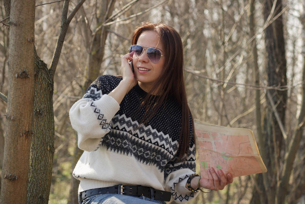 Beautiful woman with map and phone in the hands in the forest, soft focus background - Zdjęcie, obraz