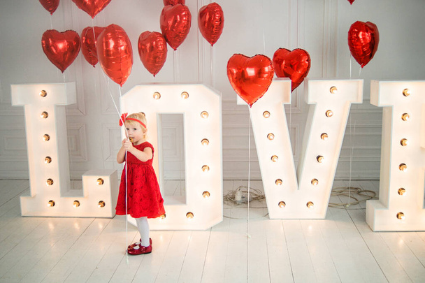 Valentinstag-Konzept. kleines Mädchen in rotem Kleid neben großen Buchstaben mit der Aufschrift Liebe und mit roten Kugeln in Herzform. Wortliebe. - Foto, Bild