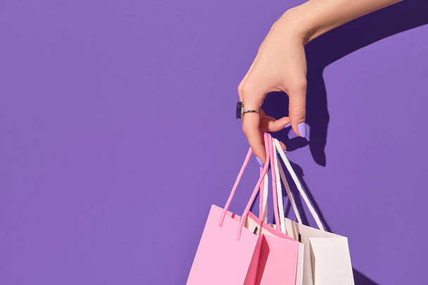 Womans hand holding paper shopping bags on purple background. Shopping sale delivery concept - Photo, Image