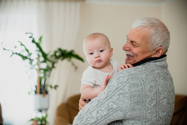 Starszy mężczyzna trzyma wnuczkę. Szczęśliwy dziadek z małą dziewczynką w ramionach. Koniec samoizolacji i spotkania z krewnymi w rodzinnej atmosferze na święta. - Zdjęcie, obraz