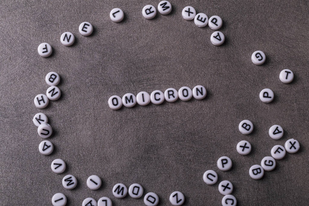 las palabras covid, omicron, están escritas en letras sobre un fondo gris. hay un montón de inscripciones de juguetes cerca - Foto, imagen
