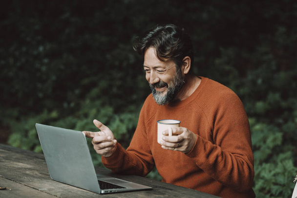Adult hipster bearded man enjoying video call conference outdoors in the nature using laptop computer. Concept of modern people and digital nomad smart working job activity outdoors - Foto, immagini