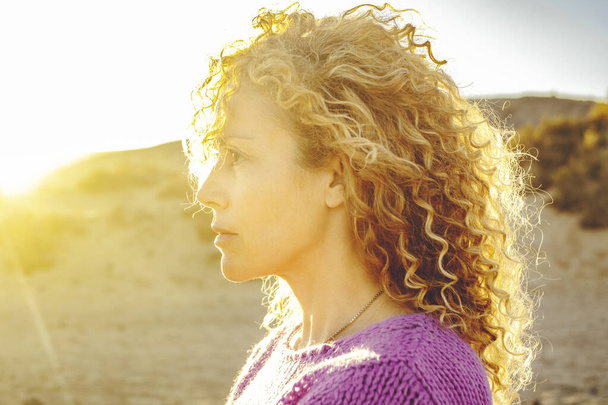 Sunset woman portrait looking serious. Curly blonde long hair female people enjoy golden sun light. Adult lady face expression. - Foto, afbeelding