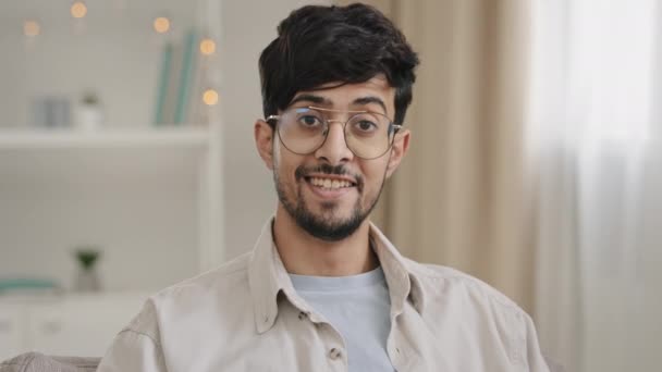 Male portrait close-up bearded face millennial arabic indian man guy with glasses looking at camera smiling waving nods head answering yes positive decision agreement support approval sitting at home - Video