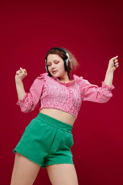 energetic young girl in green shorts listening to music Red background unaltered - 写真・画像