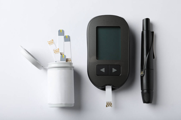 Digital glucometer, lancet pen and test strips on white background, flat lay. Diabetes control - Фото, изображение