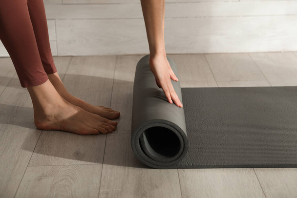 Woman rolling black yoga mat on floor indoors, closeup - Fotó, kép