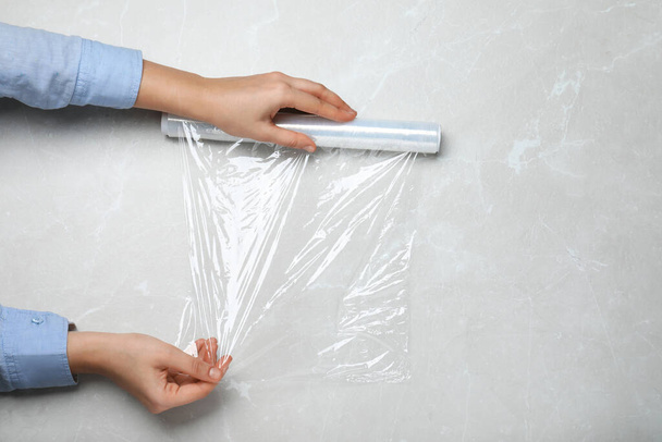 Woman with roll of stretch wrap at light grey table, top view - Photo, Image