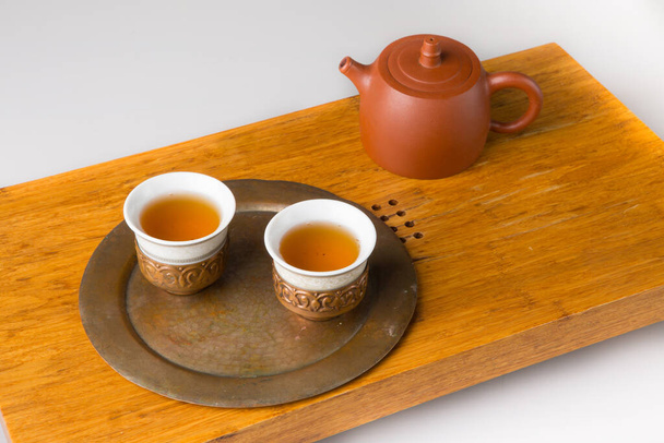 Керамічний чайник і три традиційні чашки для східного чаювання на дерев'яному столі для чайних церемоній на білому тлі. Чашки наповнені свіжозвареним зеленим чаєм
. - Фото, зображення