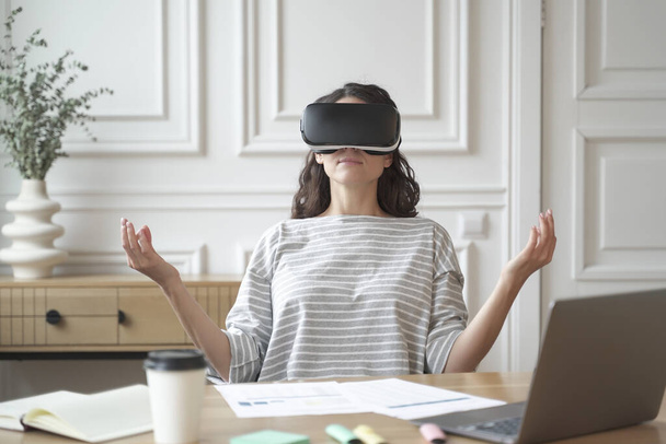 Peaceful woman employee meditating in glasses of virtual reality, sitting in zen pose at workplace - Foto, immagini