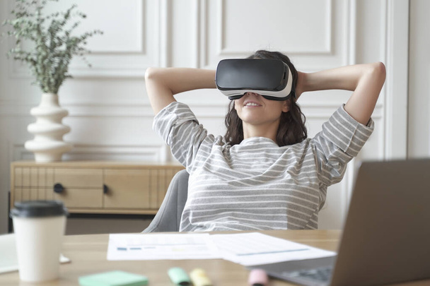 Ontspannen jonge vrouw kantoormedewerker in VR-headset of helm kijken in 360 graden video of film - Foto, afbeelding