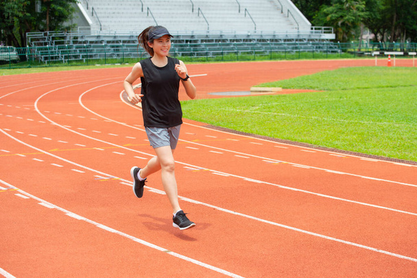 Портрет молодой счастливой спортсменки бегущей по беговой дорожке на стадионе. Беговая дорожка - это резиновая искусственная беговая дорожка для легкой атлетики. - Фото, изображение