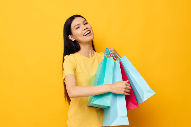 Portrait Asian beautiful young woman in a yellow T-shirt with multicolored shopping bags studio model unaltered - Fotoğraf, Görsel