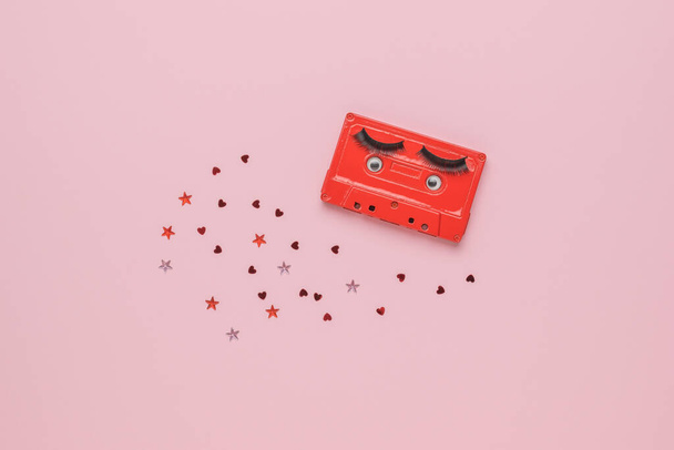Una grabadora de cinta roja y pequeños corazones dispersos sobre un fondo rosa. Imagen creativa. El concepto de grabación de sonido analógico. Puesta plana. - Foto, imagen
