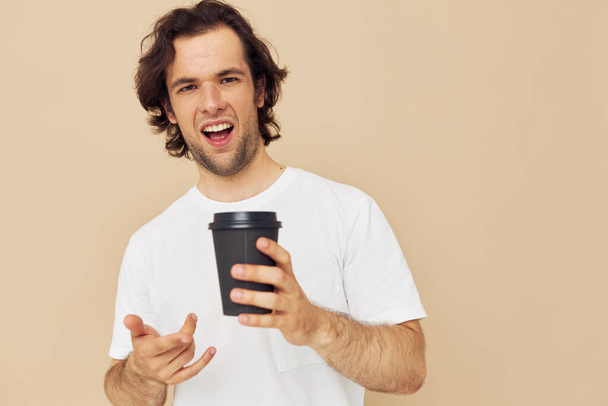 Cheerful man in a white T-shirt with a black glass in hand beige background - Foto, imagen