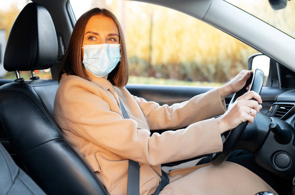 New social rules due to pandemic. Young woman wearing medical mask driving a car - Fotó, kép