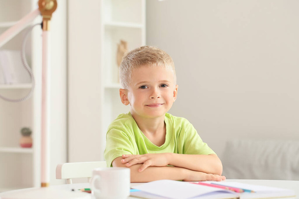 Симпатичный маленький мальчик сидит за столом в комнате - Фото, изображение