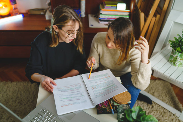 two women young caucasian female student sitting at home with her mentor teacher looking to the notebook explaining lesson study preparing for exam learning education concept real people copy space - Fotó, kép