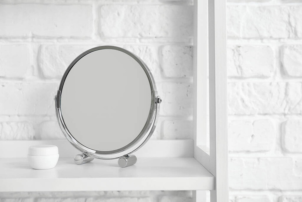 Дзеркало і баночка з вершками на полиці біля білої цегляної стіни
 - Фото, зображення