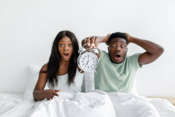 Shocked funny young african american woman and husband with open mouths overslept, wake up after night sleep - Фото, изображение