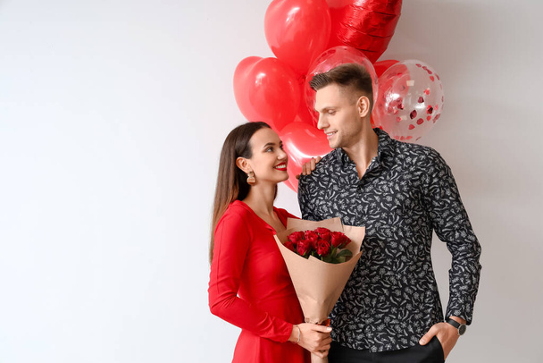 Happy young couple with bouquet of flowers and balloons on light background. Valentine's Day celebration - Fotografie, Obrázek
